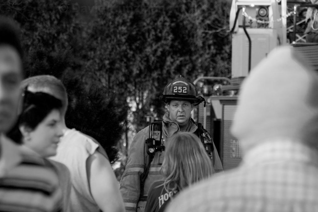 An exhausted firefighter looking at the camera through a crowd of citizens.