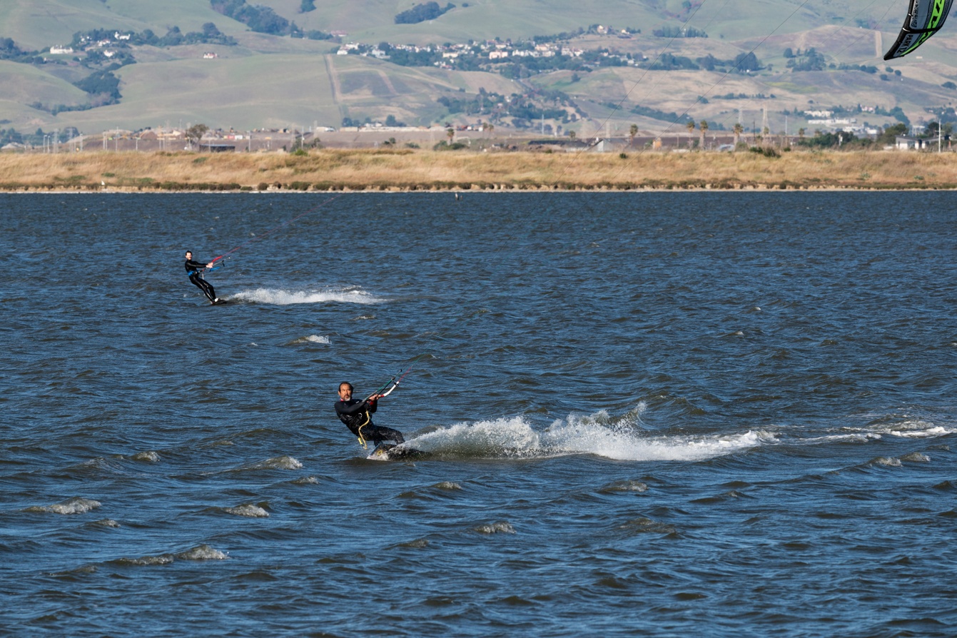 Photographs of kitesurfers having fun and performing various tricks on a clear, beautiful day.